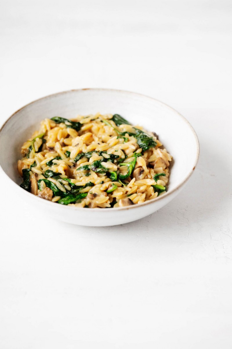 A white bowl with a pale brown rim has been filled with a mixture of small pasta and greens.