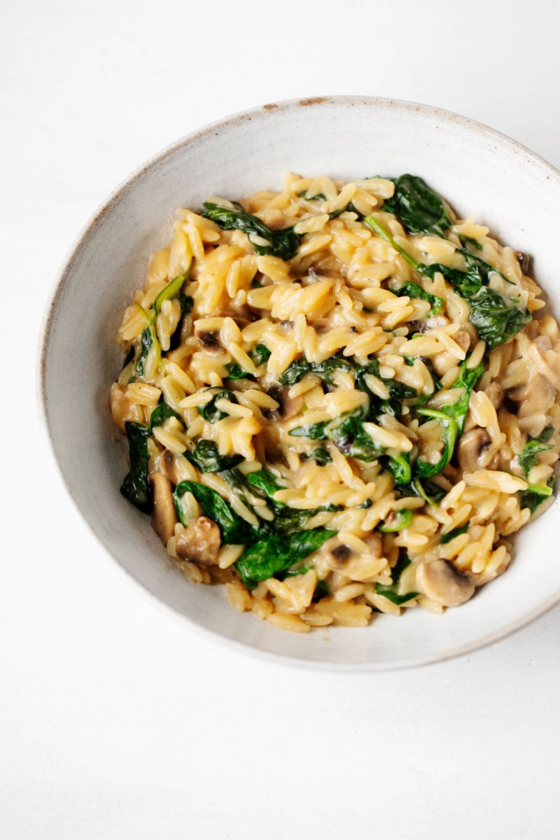 A white bowl has been filled with creamy, plant-based orzo and vegetables.