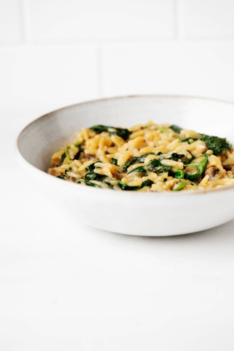 A round, white bowl has been filled with orzo and spinach. It's resting on a bright white surface.