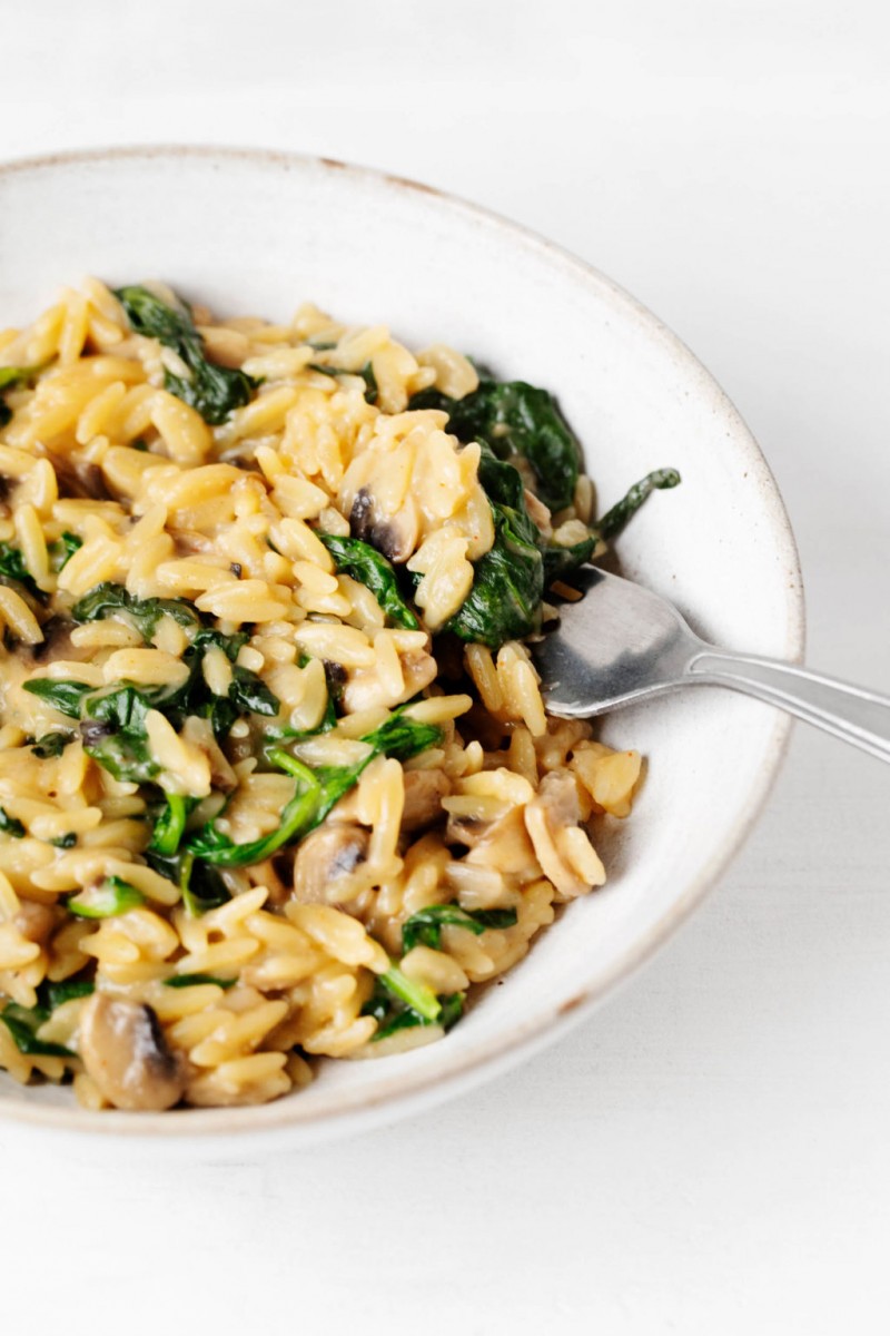 A bright white ceramic bowl has been filled with creamy, cooked small pasta and vegetables.