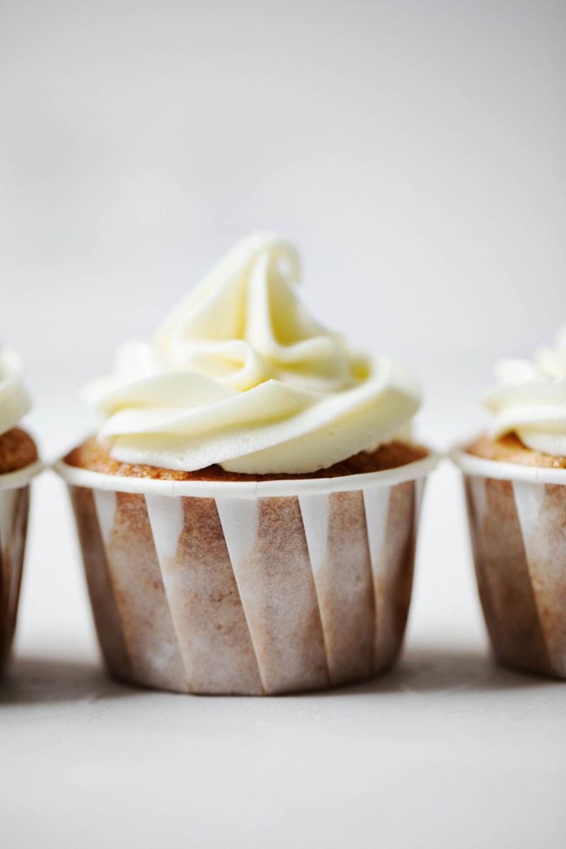 Plant based cider cupcakes with cream cheese frosting, lined up in a neat row.