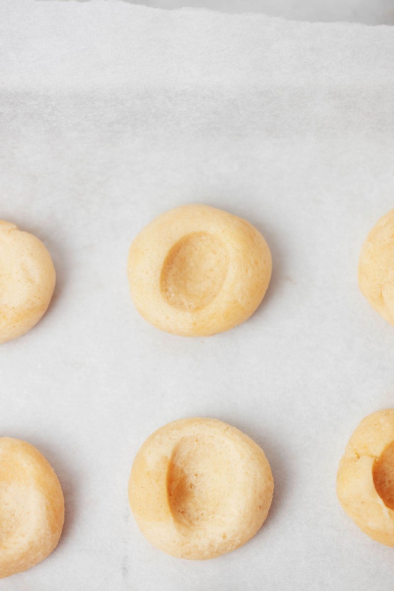 Several rough pieces of cookie dough rest on a lined baking sheet.