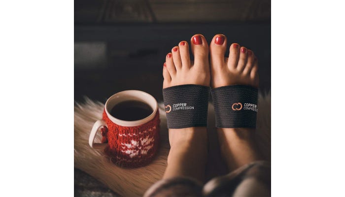 A woman's feet wearing black compression sleeves around her arches with a coffee mug to the left.