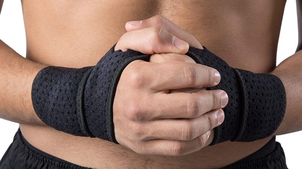 A close up of a man's hands clasped together in front of his torso while wearing a black wrist brace on both hands.