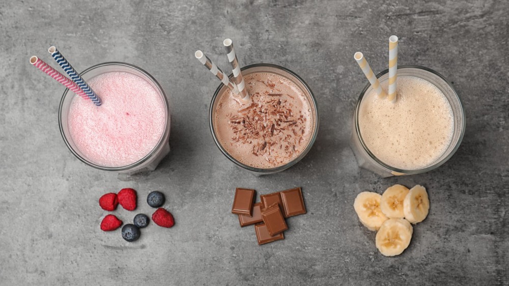 Glasses with different protein shakes and ingredients on grey background.