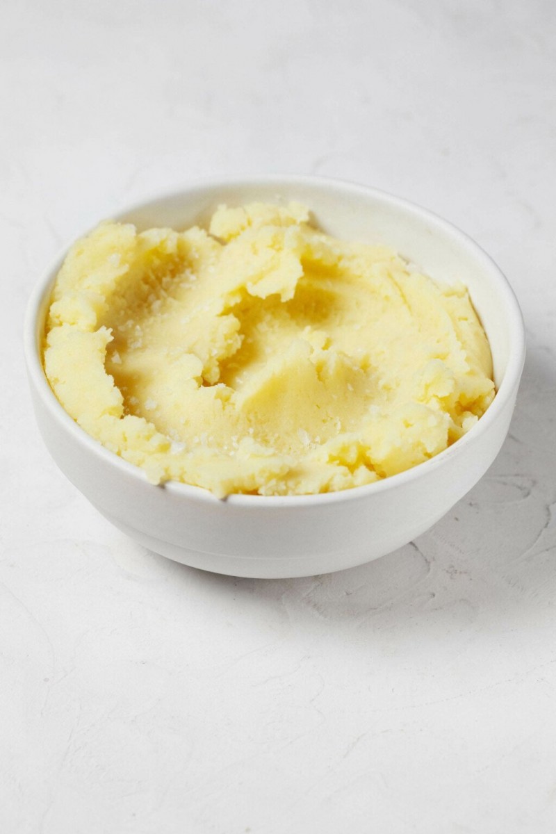 A round white bowl is filled with fluffy, smooth, and creamy vegan mashed potatoes. 