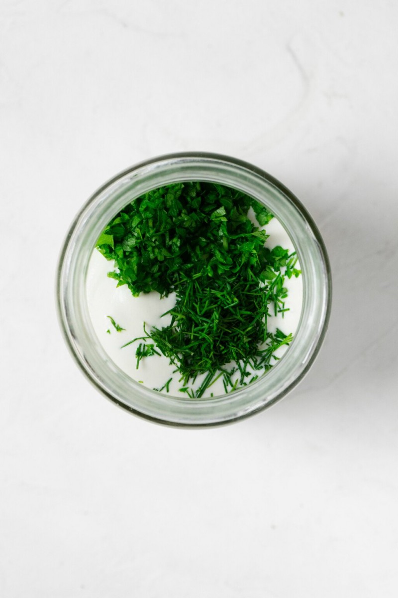 An overhead image of the round mouth of a glass jar. The jar is filled with a creamy dressing and fresh, chopped herbs.