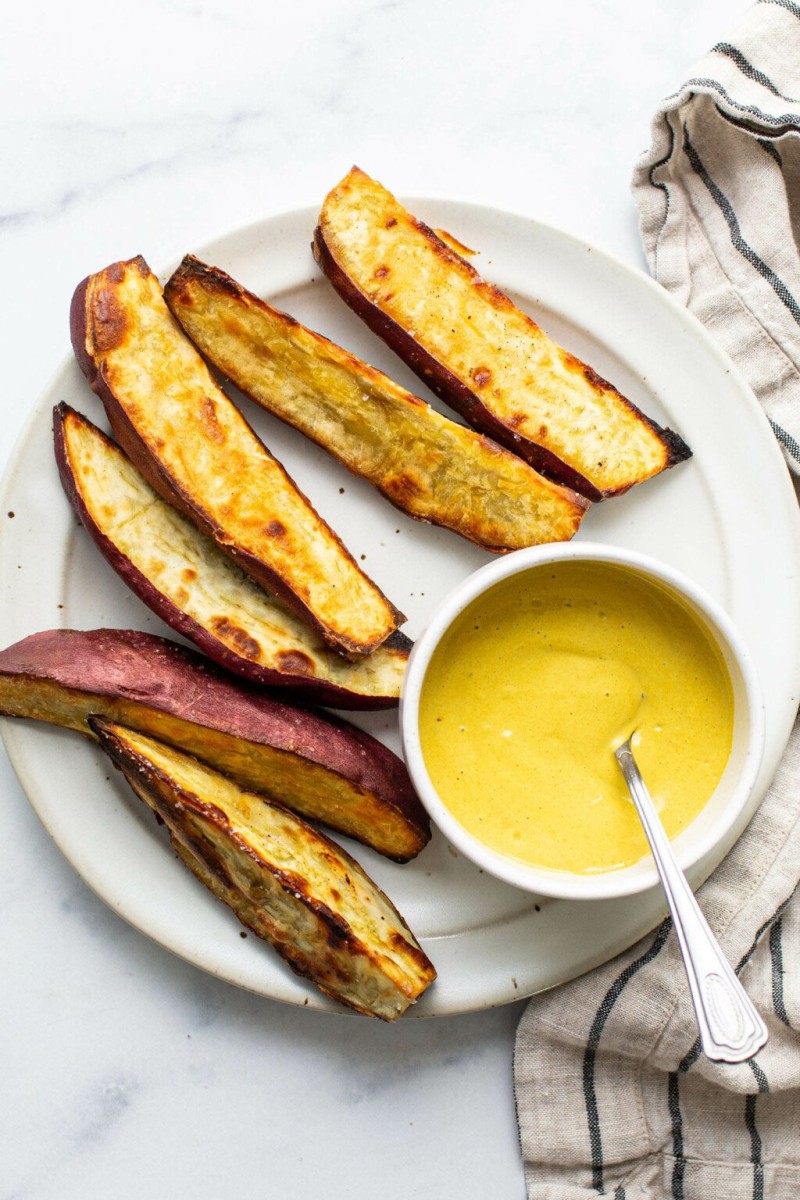 An overhead image of crispy roasted Japanese sweet potato wedges. They're arranged on a white platter with a bright yellow dipping sauce.