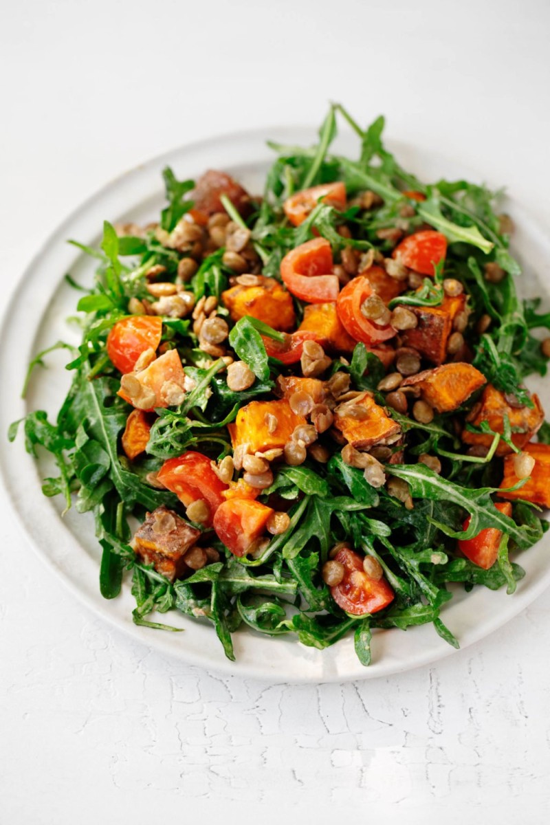 A round white plate has been covered in a colorful, creamy lentil tahini sweet potato salad.