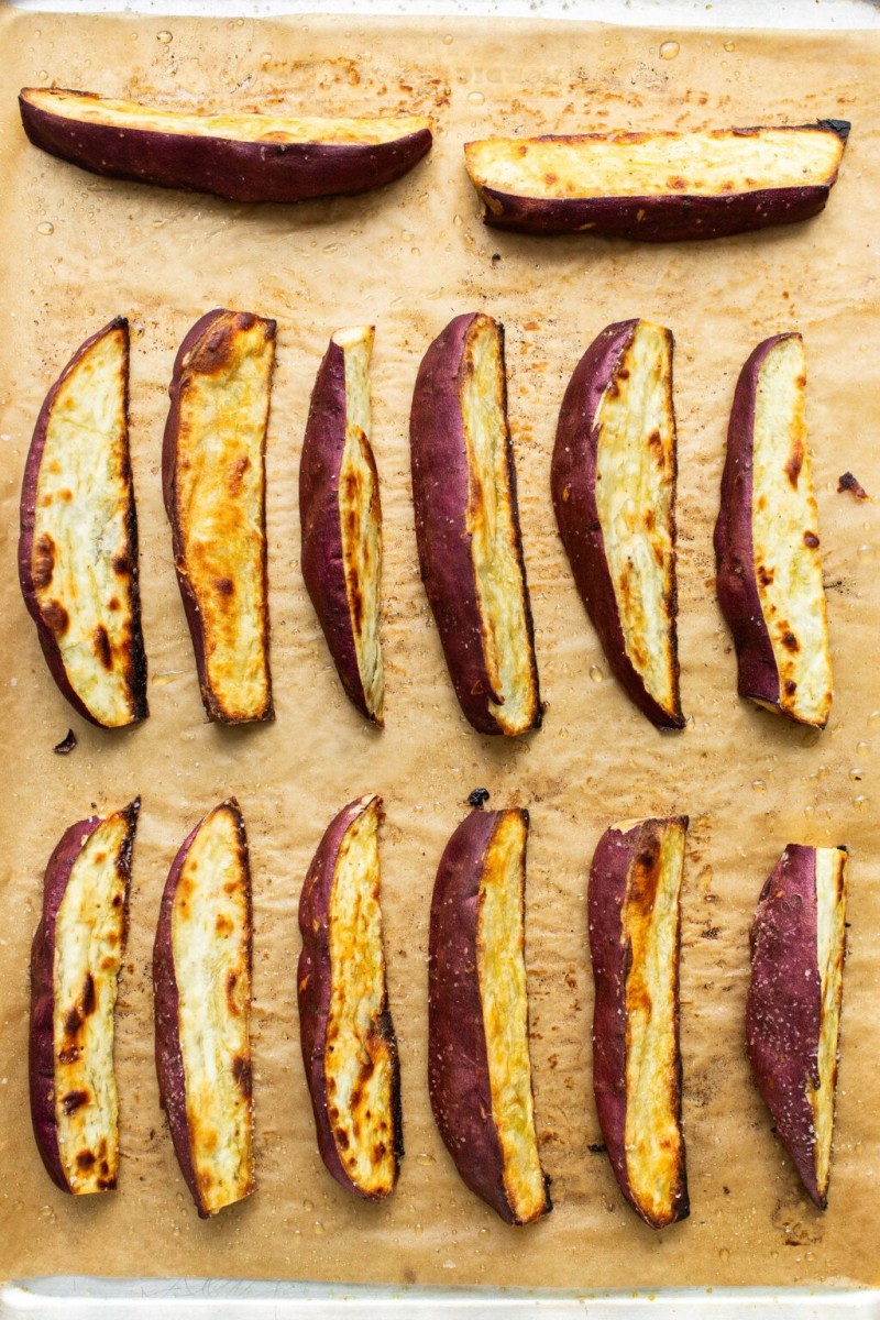 Wedges of roasted Japanese sweet potato are arranged on a brown parchment sheet.